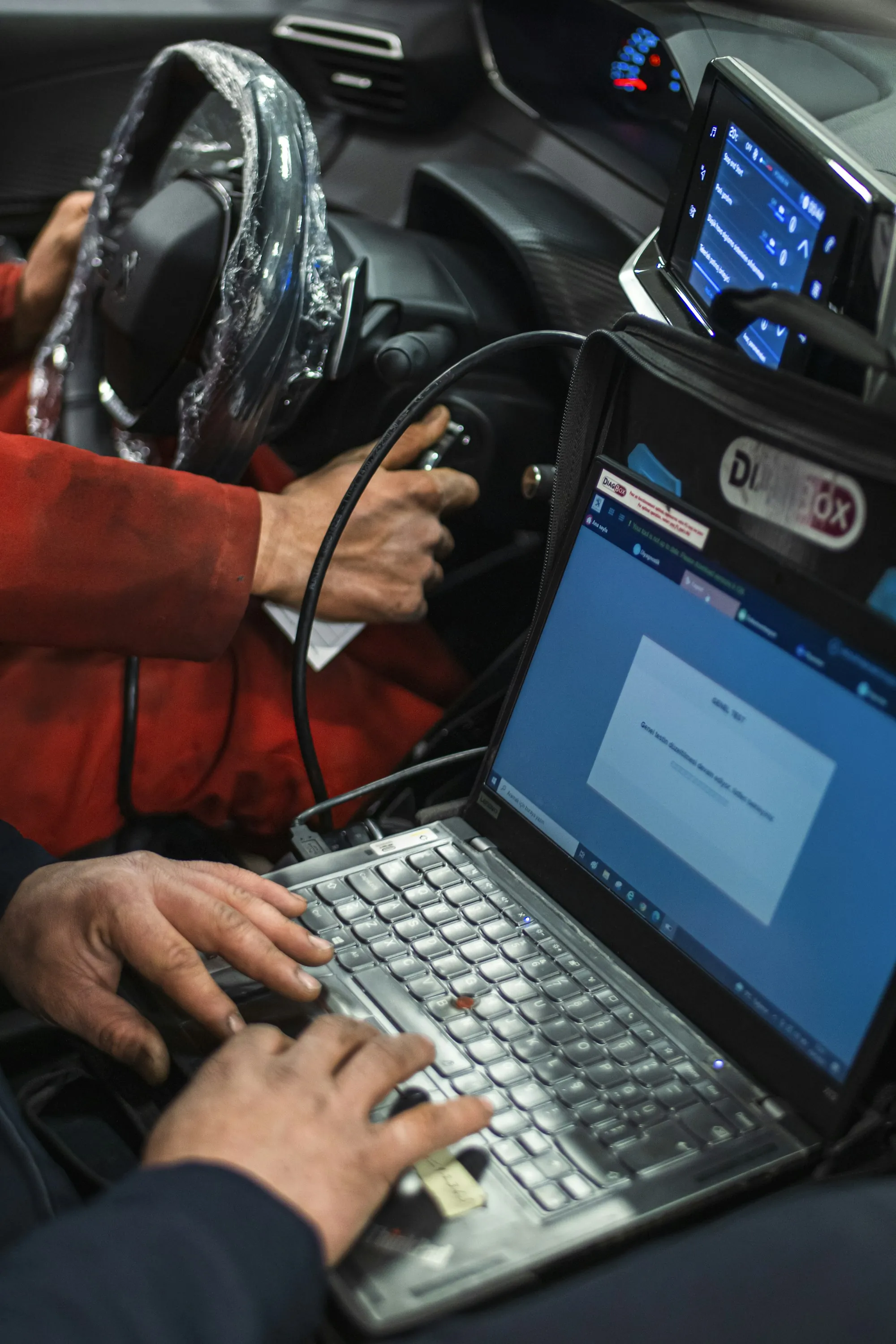 Technician typing on a laptop connected to a vehicle's diagnostic port