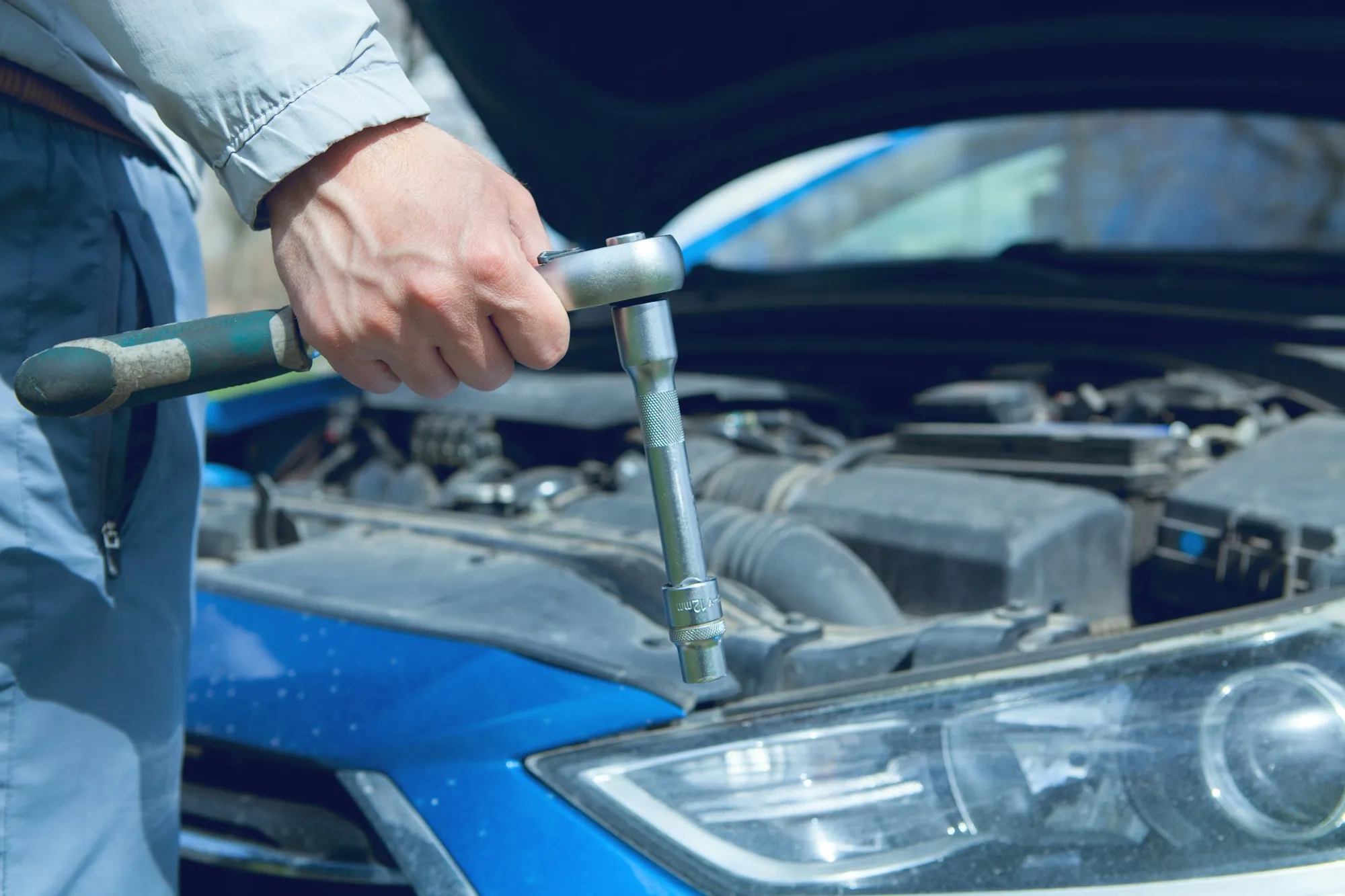 Technician tightening a fitting under the hood of a blue car