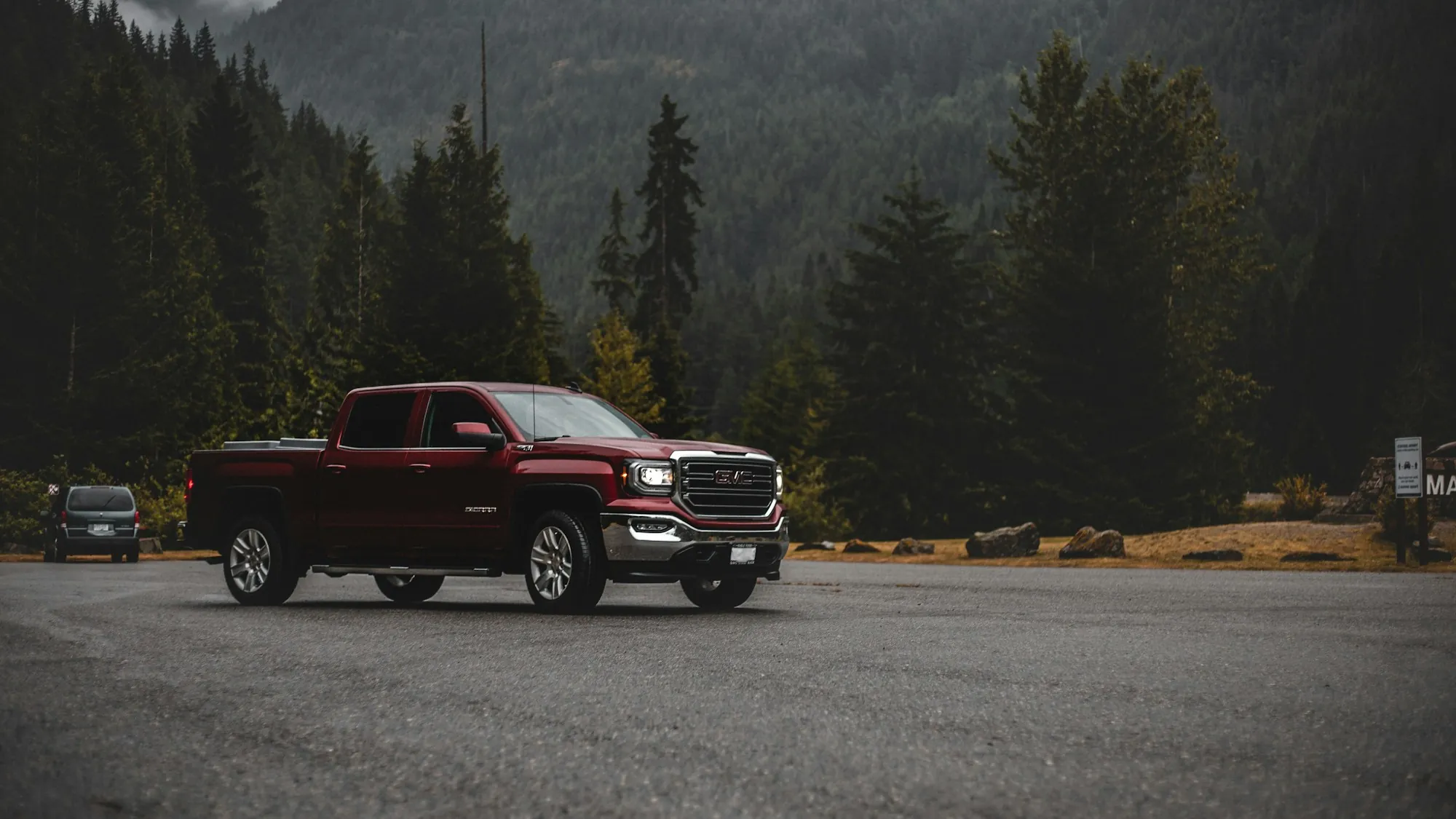 Red pickup truck on a mountain road lined with pine trees
